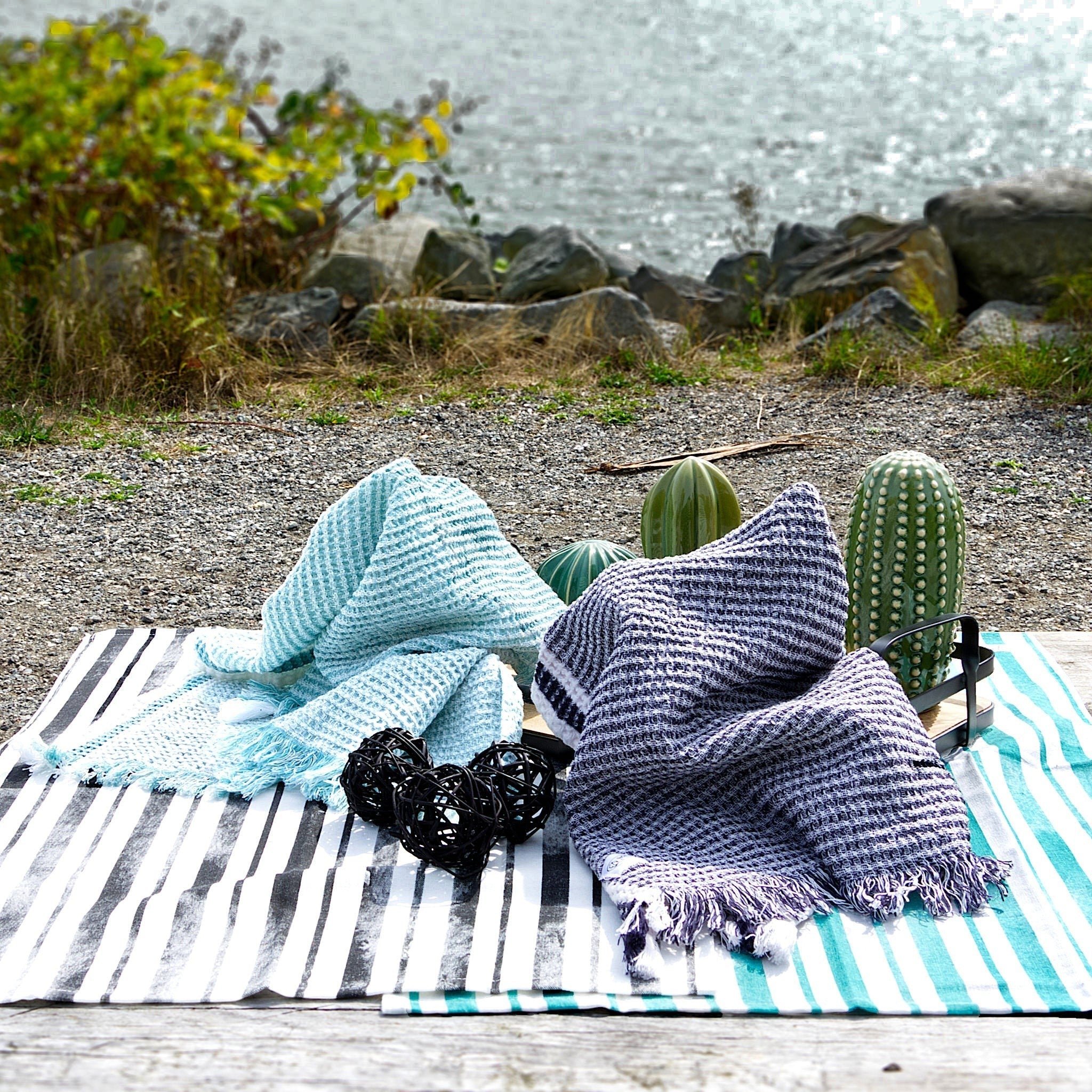 Two textured waffle kitchen towels, one blue and one purple, on a striped kitchen towel with cacti in a natural setting from Hem And Tassel