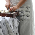 woman working in kitchen wearing plain white apron with black and white 'stems' print design on pocket and hems - from Hem And Tassel