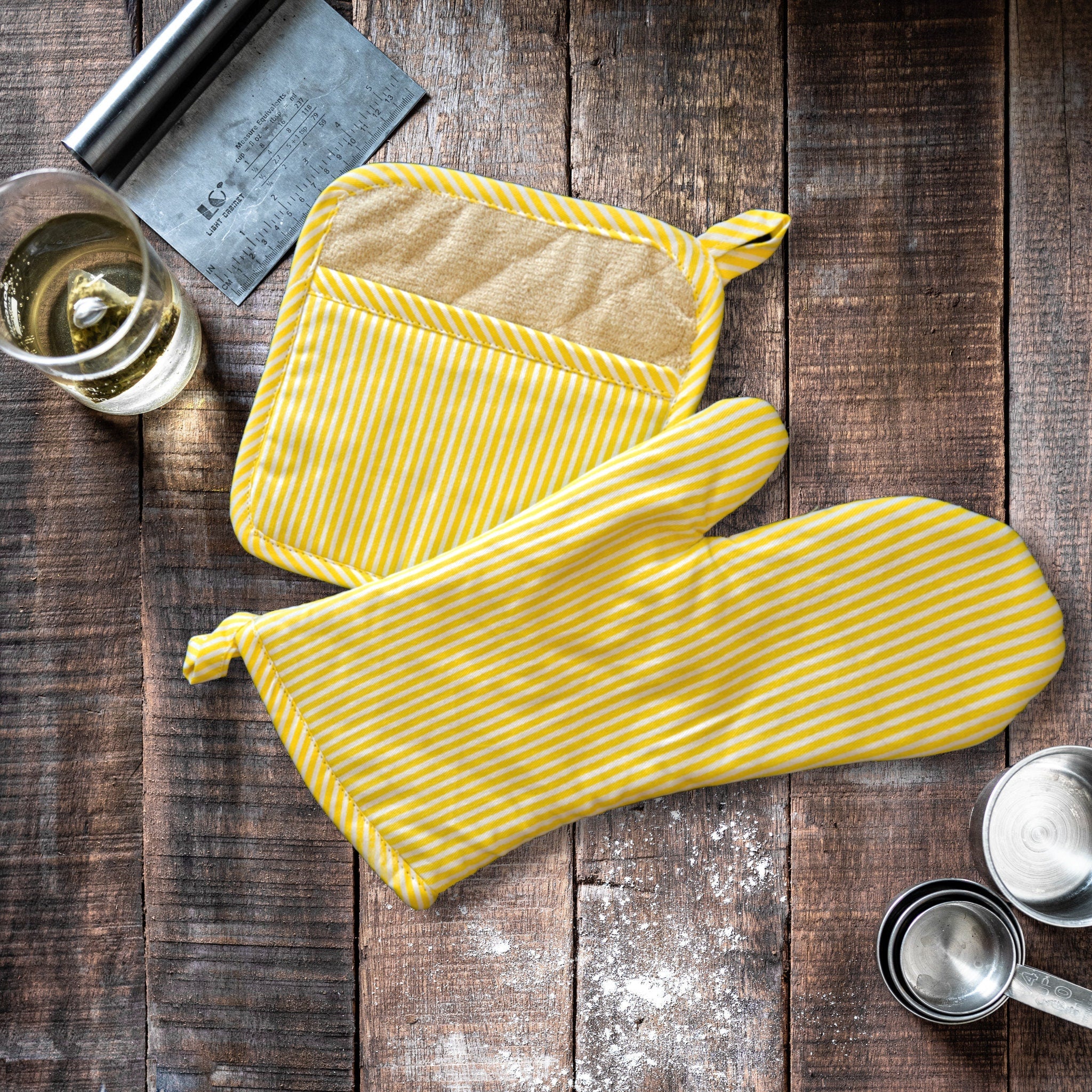 Yellow striped pot holder and oven mitt on a wooden surface with a glass of white wine.