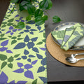 textured slub-cotton table runner with decorative edging, in celebration design, with matching turf dinner napkins and place setting on wooden dining table - from Hem And Tassel