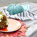 Teal pumpkin on a pair of distressed stripe print towels, on a wooden surface with a plate, leaves, and decorative items from Hem And Tassel 