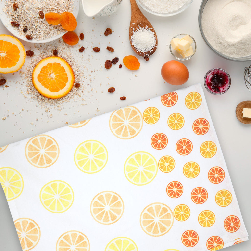 Colorful lemon and orange patterned faded fruit kitchen towel on a white surface with baking ingredients from Hem And Tassel