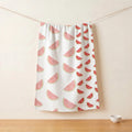 A white pure cotton kitchen towel featuring a watermelon slice pattern, hanging from a string against a beige wall with a wooden tabletop and a small bowl below from Hem And Tassel