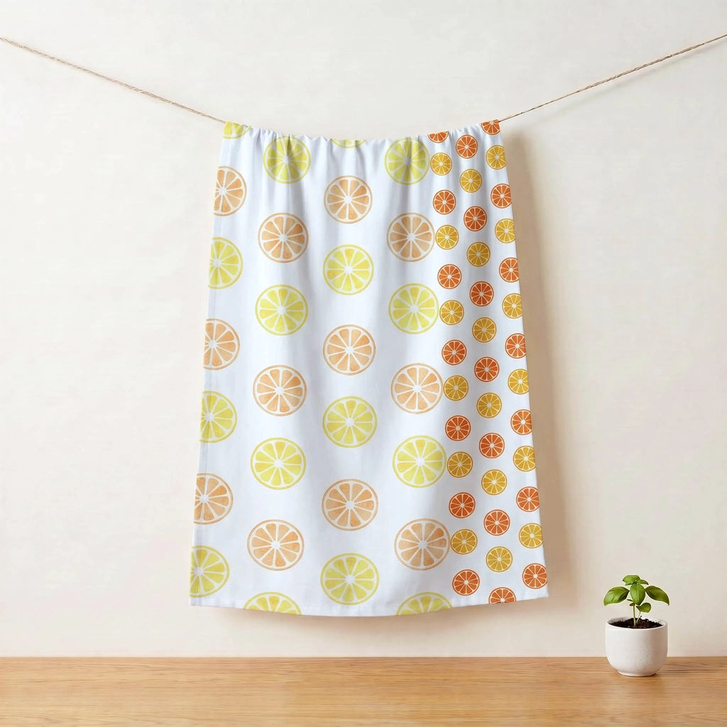 A white pure cotton kitchen towel featuring a orange slice pattern, hanging from a string against a beige wall with a wooden tabletop and a small bowl below from Hem And Tassel