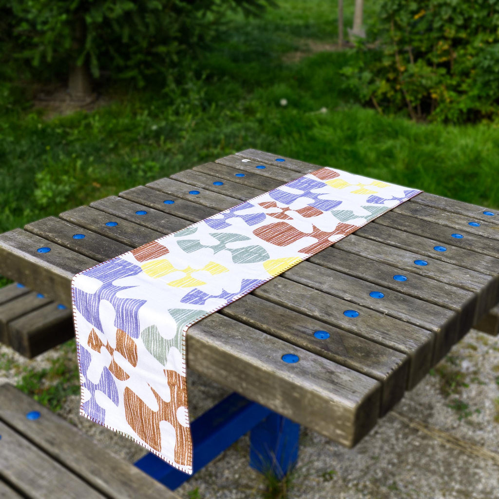 Colorful patterned Flock and flutter table runner on a wooden bench outdoors from Hem And Tassel 