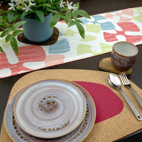 Dining table setting with Flock and flutter table runner,  plates, cutlery, and a plant on colorful placemats.