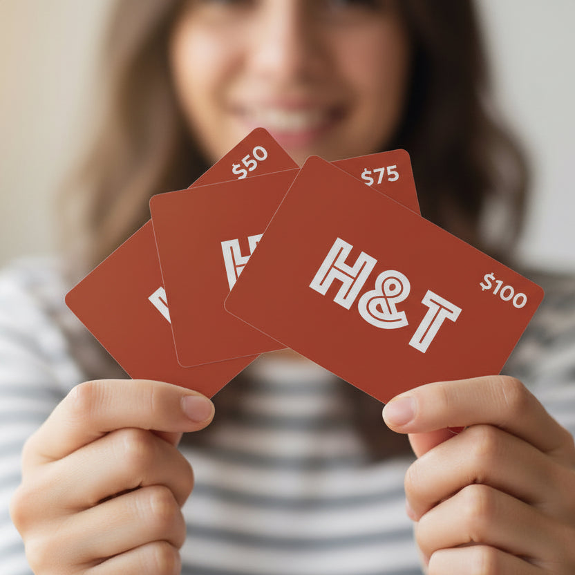 Person holding a red gift card with 'H&T' and different values of $50, $75 and $100 from Hem And Tassel 