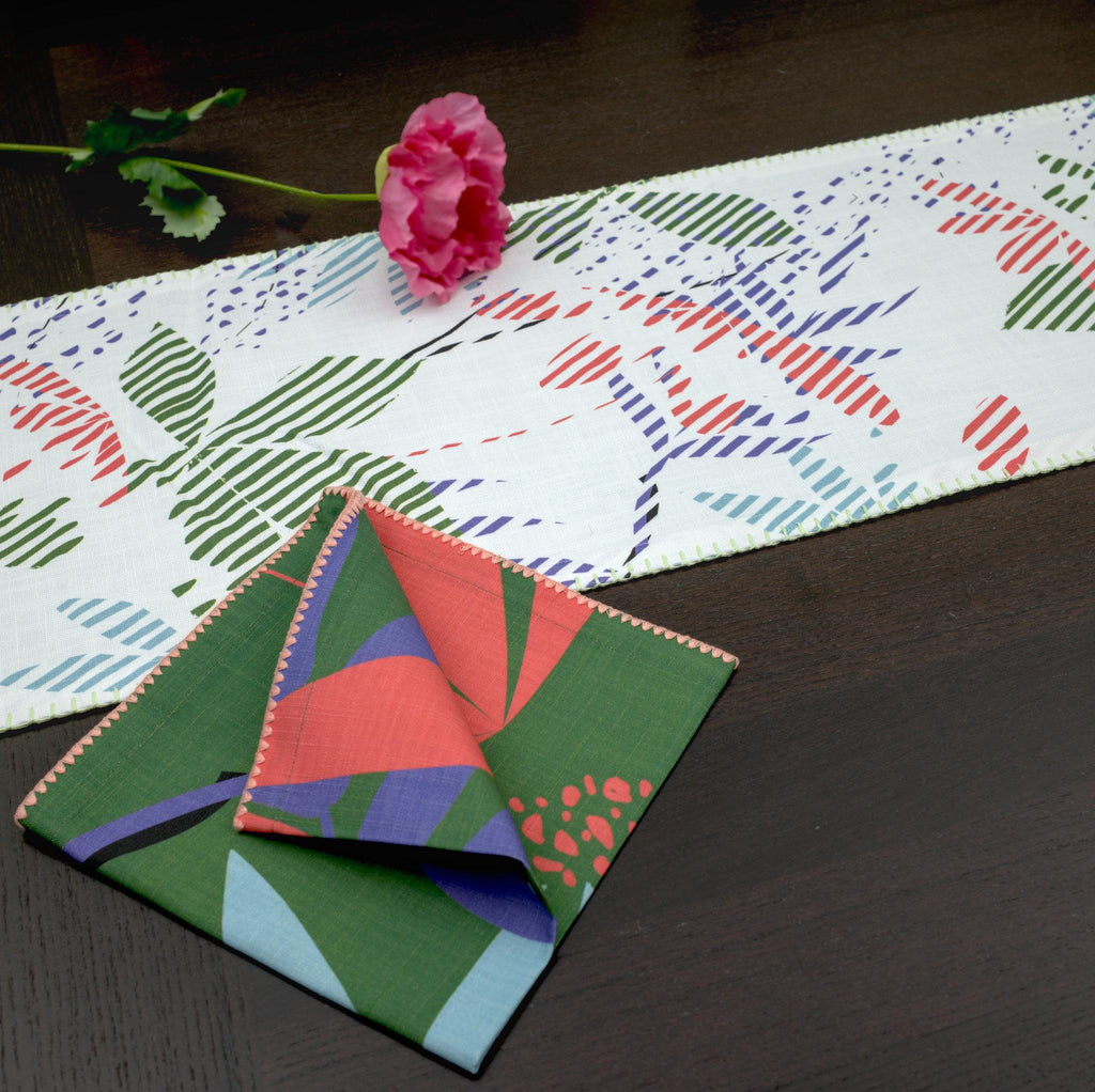 Green and pink 'pollen up' design dinner napkin of pure cotton by Hem And Tassel on a dining table with a white table runner of the same collection on a dining table