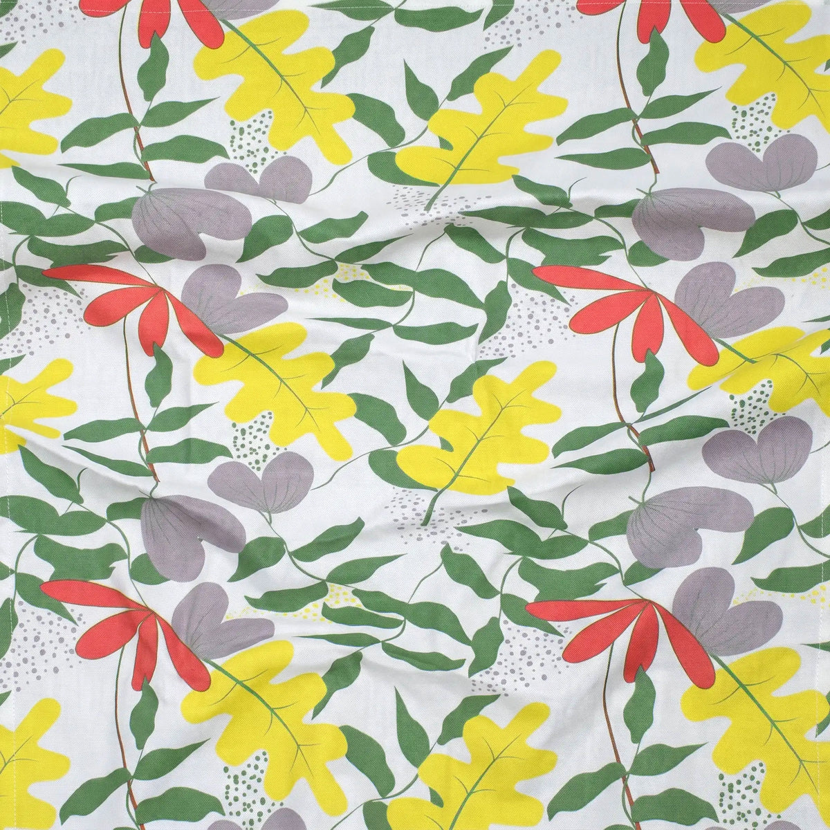 A close-up of a white cotton kitchen towel with a colorful botanical pattern featuring yellow oak leaves, green leaves, red flowers, and purple heart-shaped motifs from Hem And Tassel 