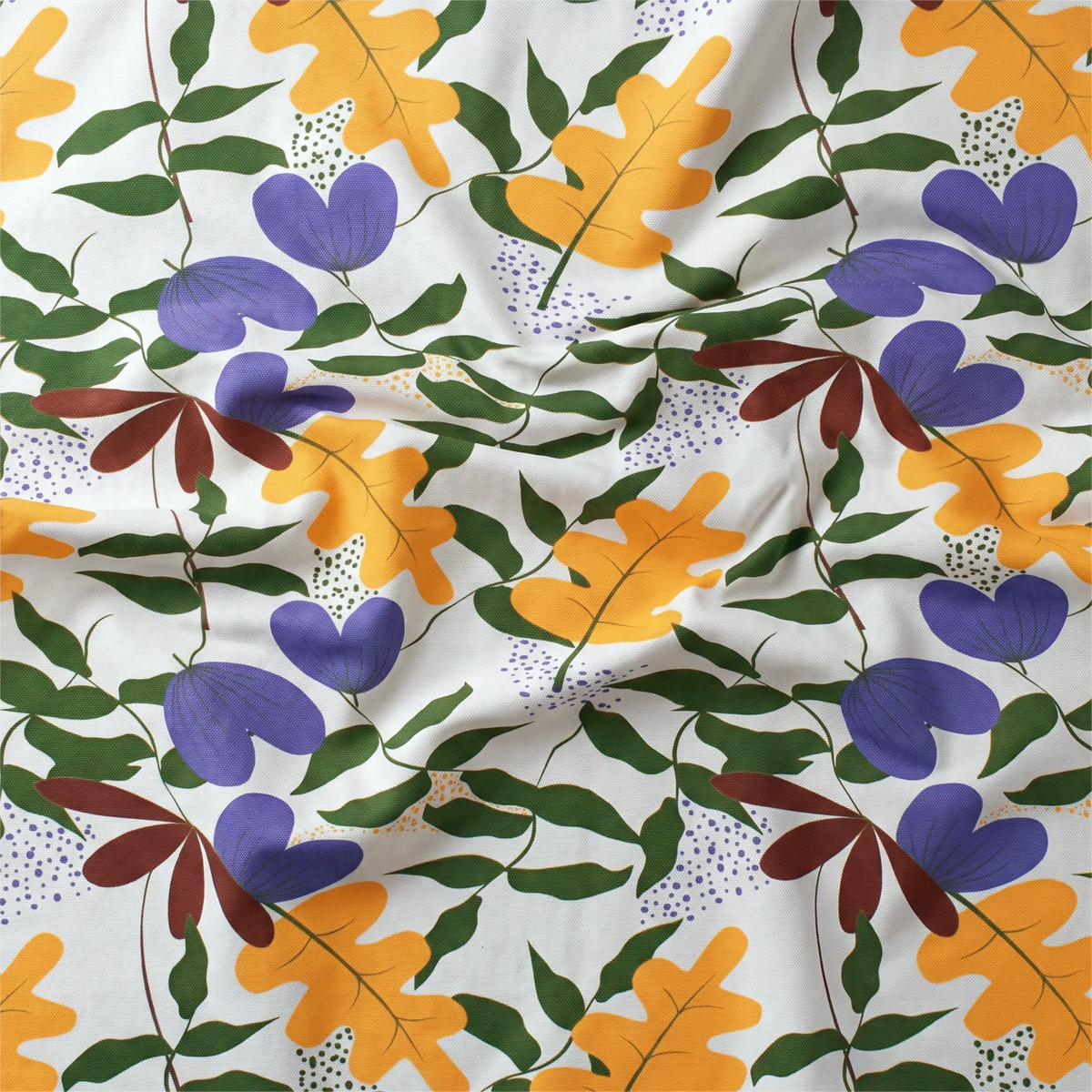 A close-up of a wrinkled white cotton kitchen towel printed with a repeating botanical pattern of purple flowers, orange oak leaves, green leaves, and small brown accents from Hem And Tassel 