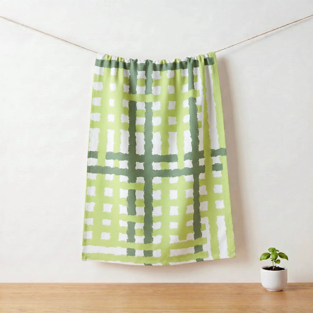 Green and white checkered cotton kitchen towel  hanging on a rod with a small plant on a wooden floor from Hem And Tassel 