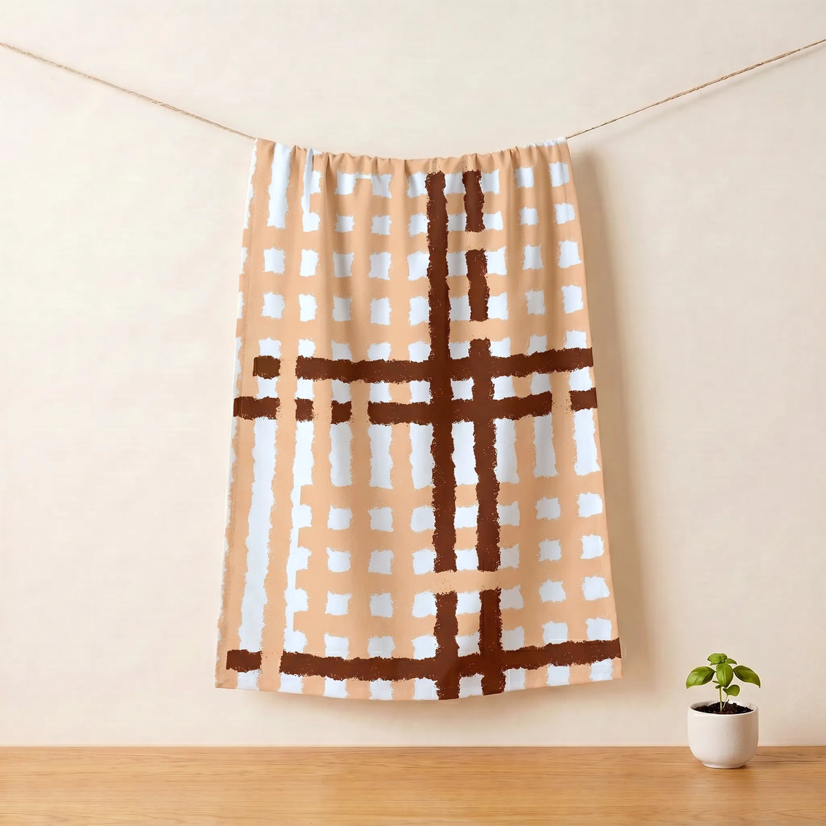 Plaid cotton kitchen towel hanging on a line against a beige wall with a plant on a wooden floor from Hem And Tassel 