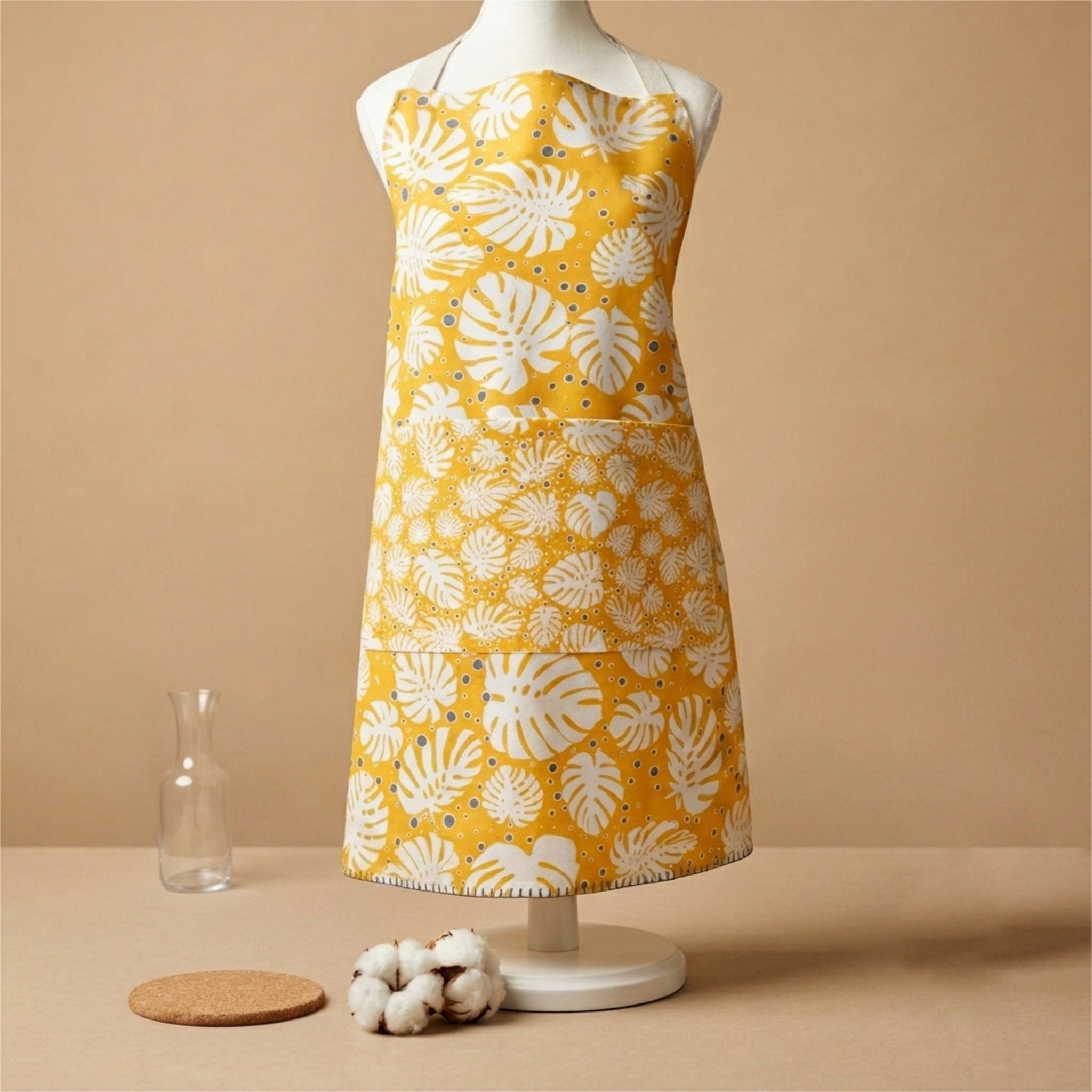 Yellow apron with white floral pattern on a mannequin against a beige background