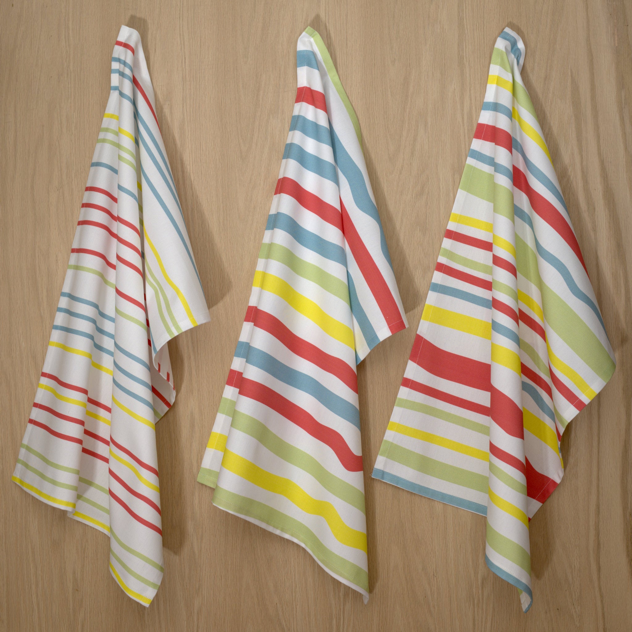 Three colorful not straight design kitchen towels for Summer  hanging on a wooden wall.
