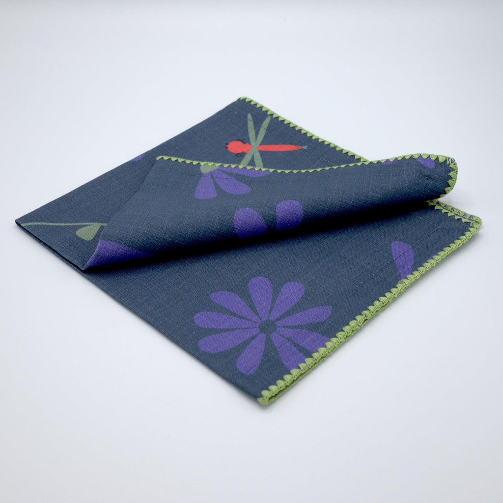 Oil and purple 'Shy Dragonfly' design cotton dinner napkin by Hem And Tassel folded on a white background