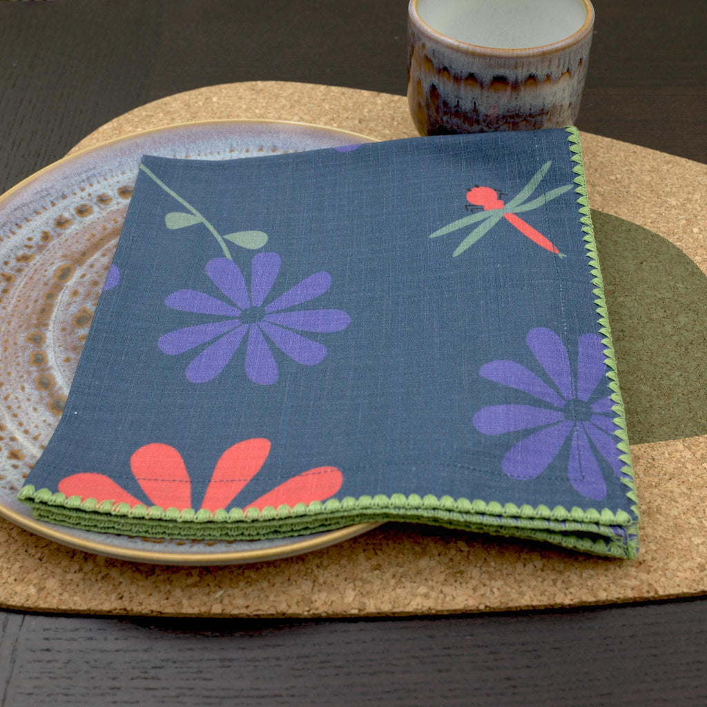 Oil and purple 'Shy Dragonfly' design cotton dinner napkin by Hem And Tassel folded on a plate and placemat