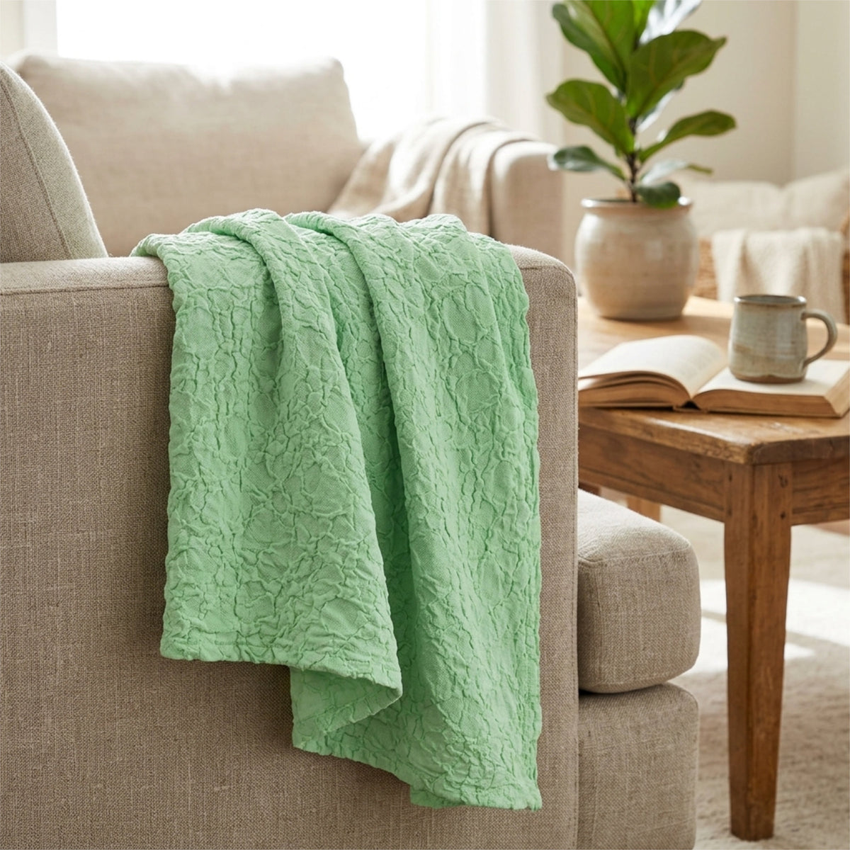A box waffle soft mint colored woven throw blanket hemmed on four sides, draped over the arm of a beige armchair in a bright, modern living room setting from Hem And Tassel 