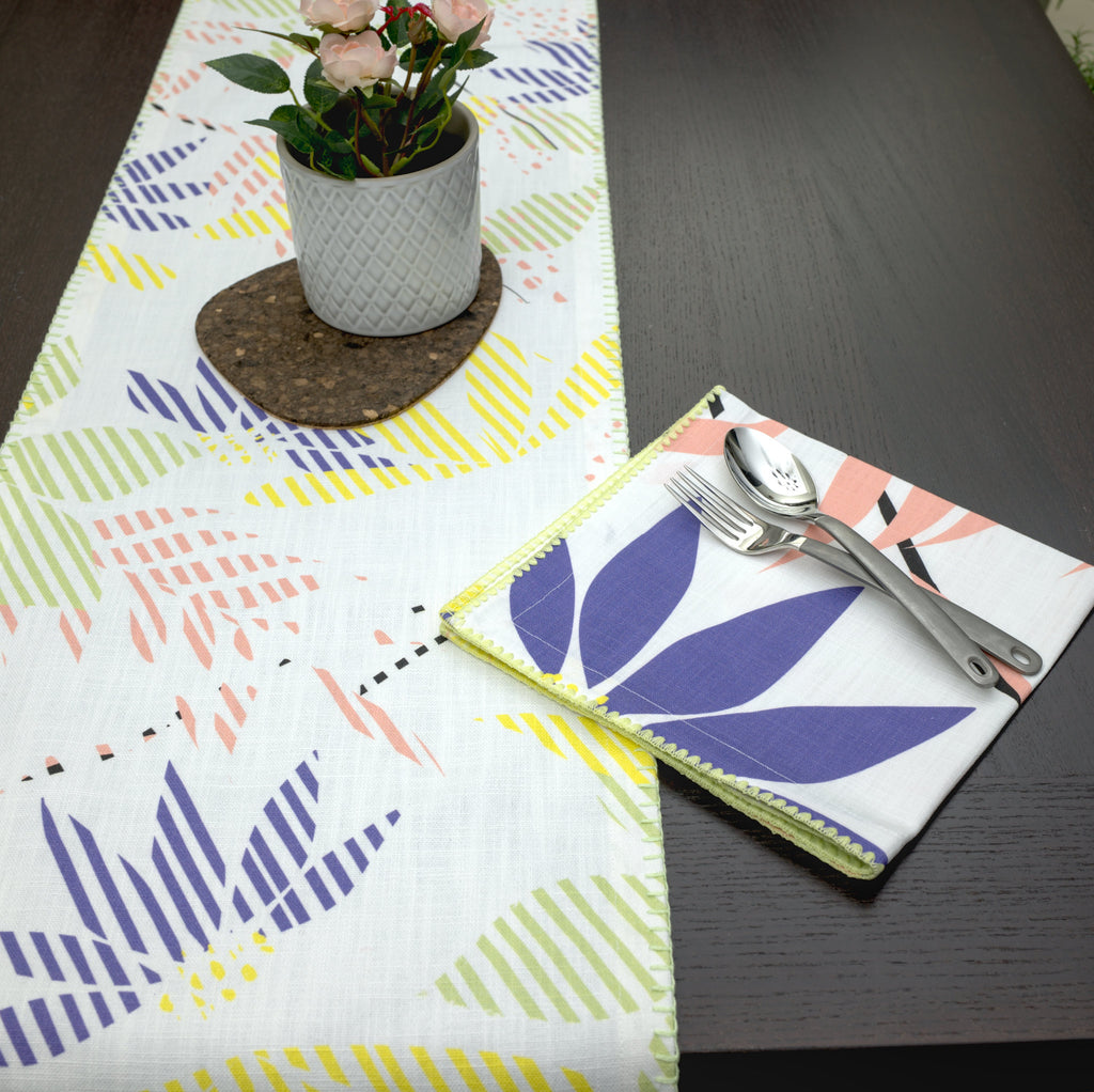Table setting with a colorful Pollen up table runner, leaf-patterned napkin, and cutlery on a dark surface.