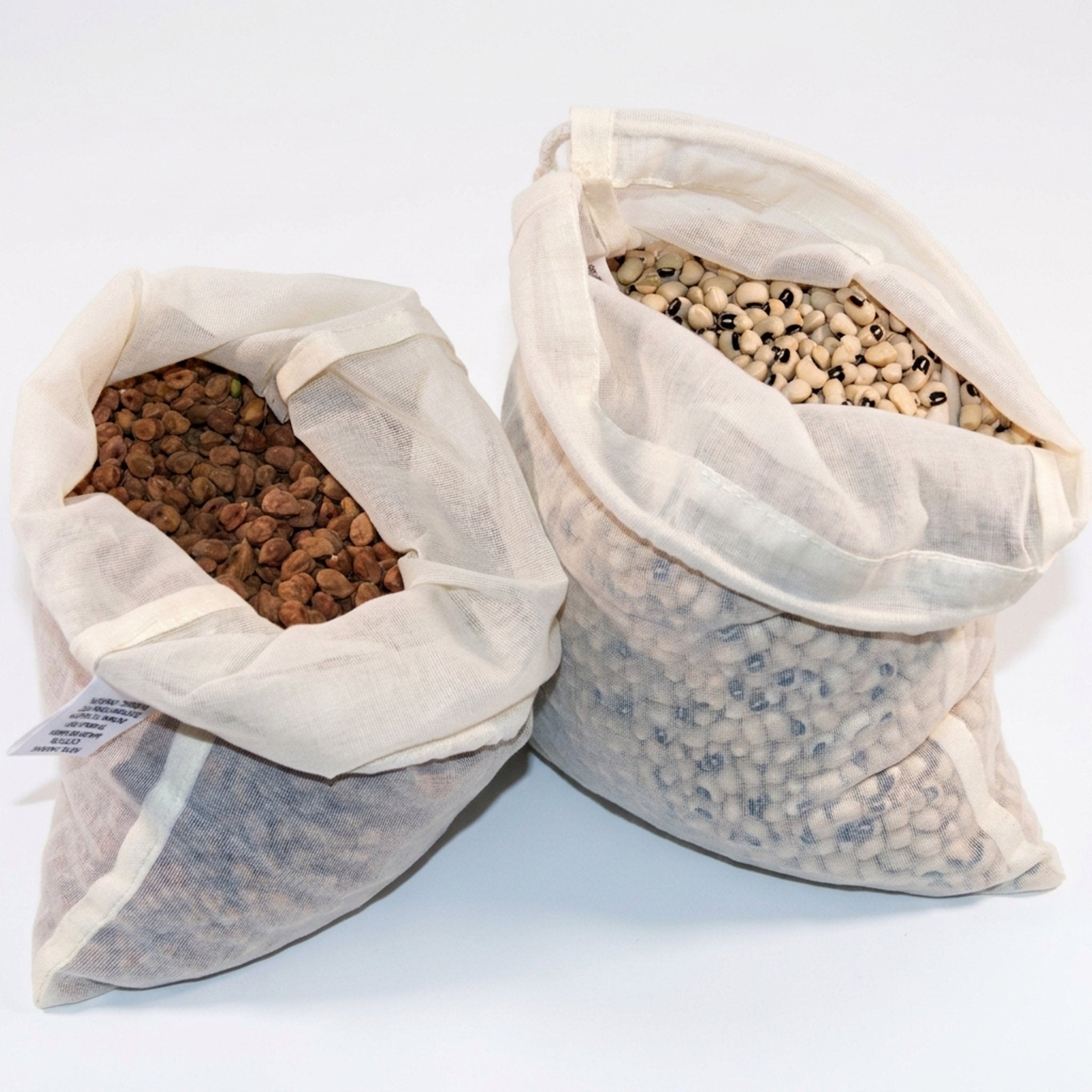 Two open off-white fine organic cotton bags filled with dried beans or seeds, photographed on a plain white studio background from Hem And Tassel 