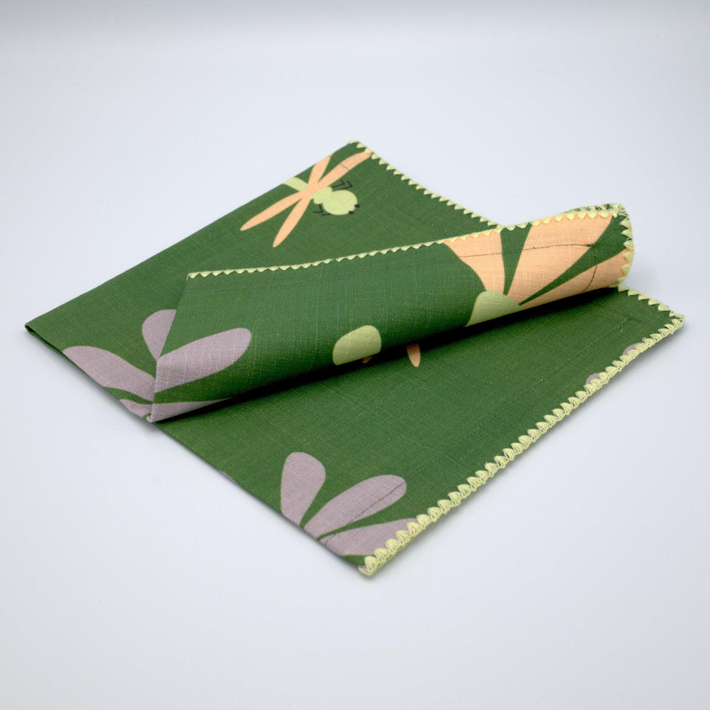 'Shy Dragonfly" design cotton napkins by Hem And Tassel, in green and buff, folded on a light grey background