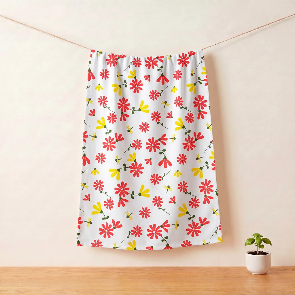 A white cotton kitchen towel with a colorful pattern of red, yellow, and orange flowers hanging on a clothesline in a minimalist room setting with a small potted plant on a wooden table from Hem And Tassel 