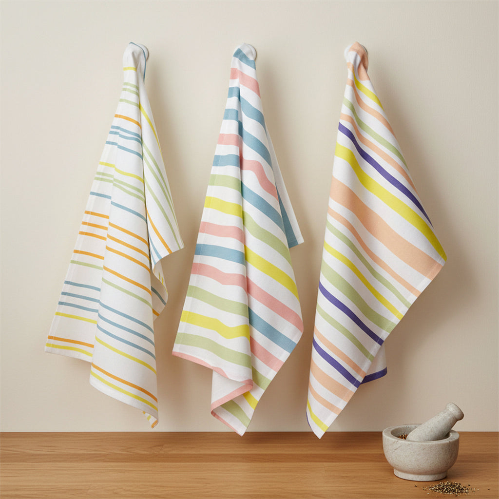 Spring colors stripes in narrow, medium and broad widths on 3 cotton kitchen towels hanging on a beige wall with a mortar and pestle and grains on a wood counter below from Hem And Tassel 