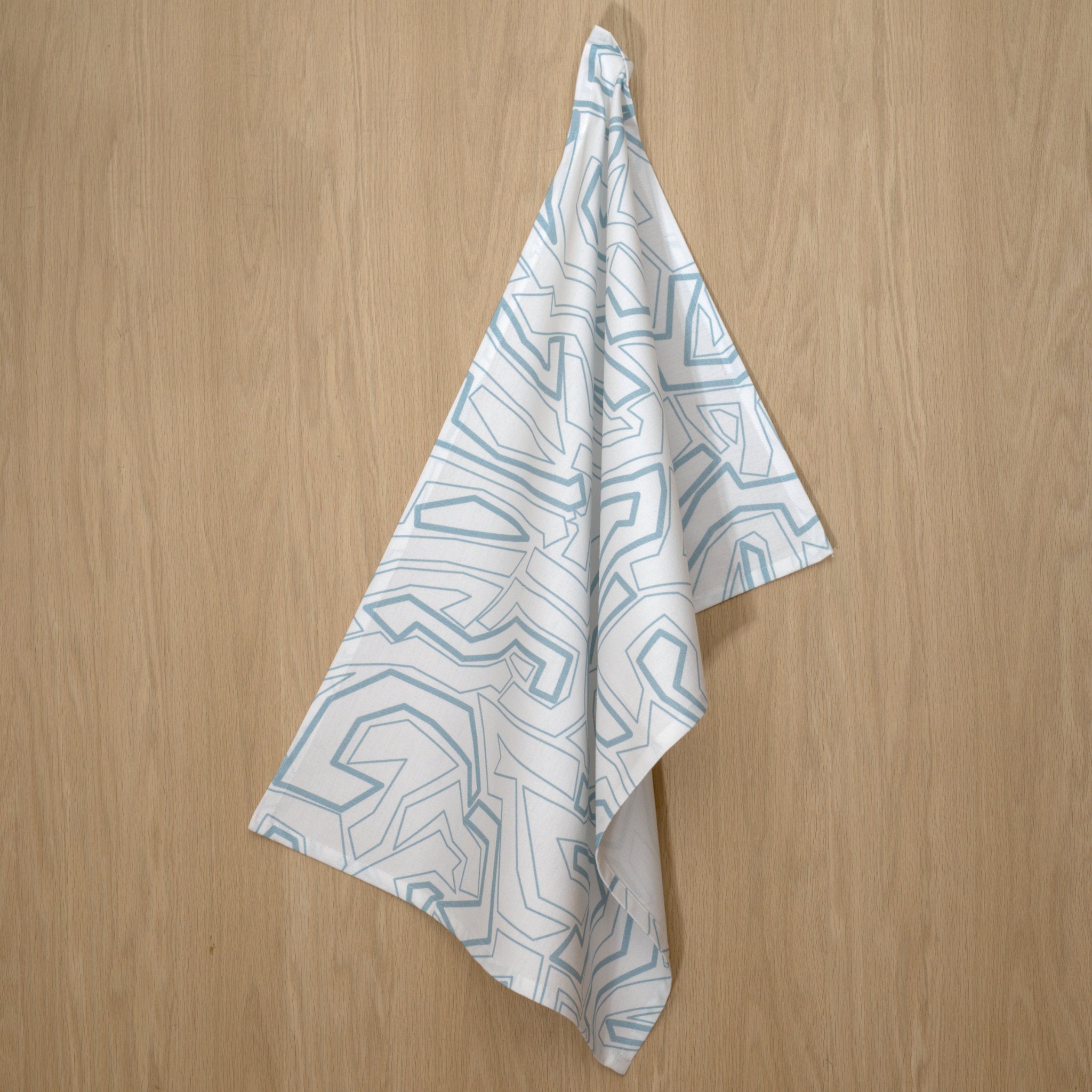 Hanging towel with geometric squiggles pattern with light blue lines on a wooden surface