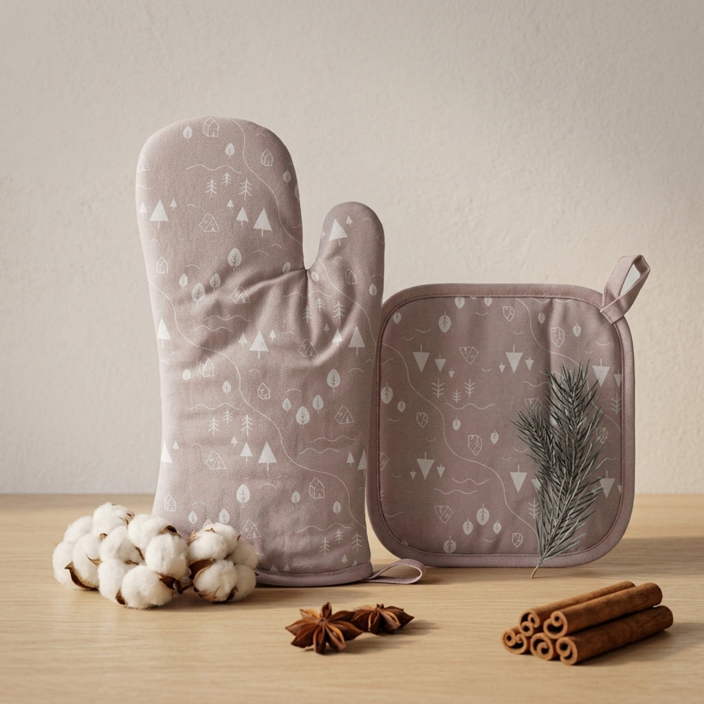 A matching oven mitt and pot holder set in a dusty mauve color with a white forest tree pattern, styled on a light wood surface with cotton bolls, star anise, cinnamon sticks, and a pine sprig against a neutral beige background from Hem And Tassel