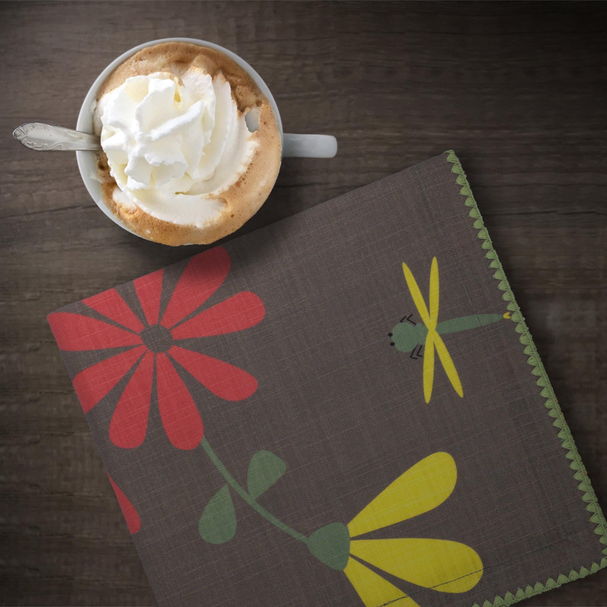 Cup of coffee with whipped cream on a wooden surface next to winter and pink 'Shy Dragonfly' design cotton dinner napkin by Hem And Tassel