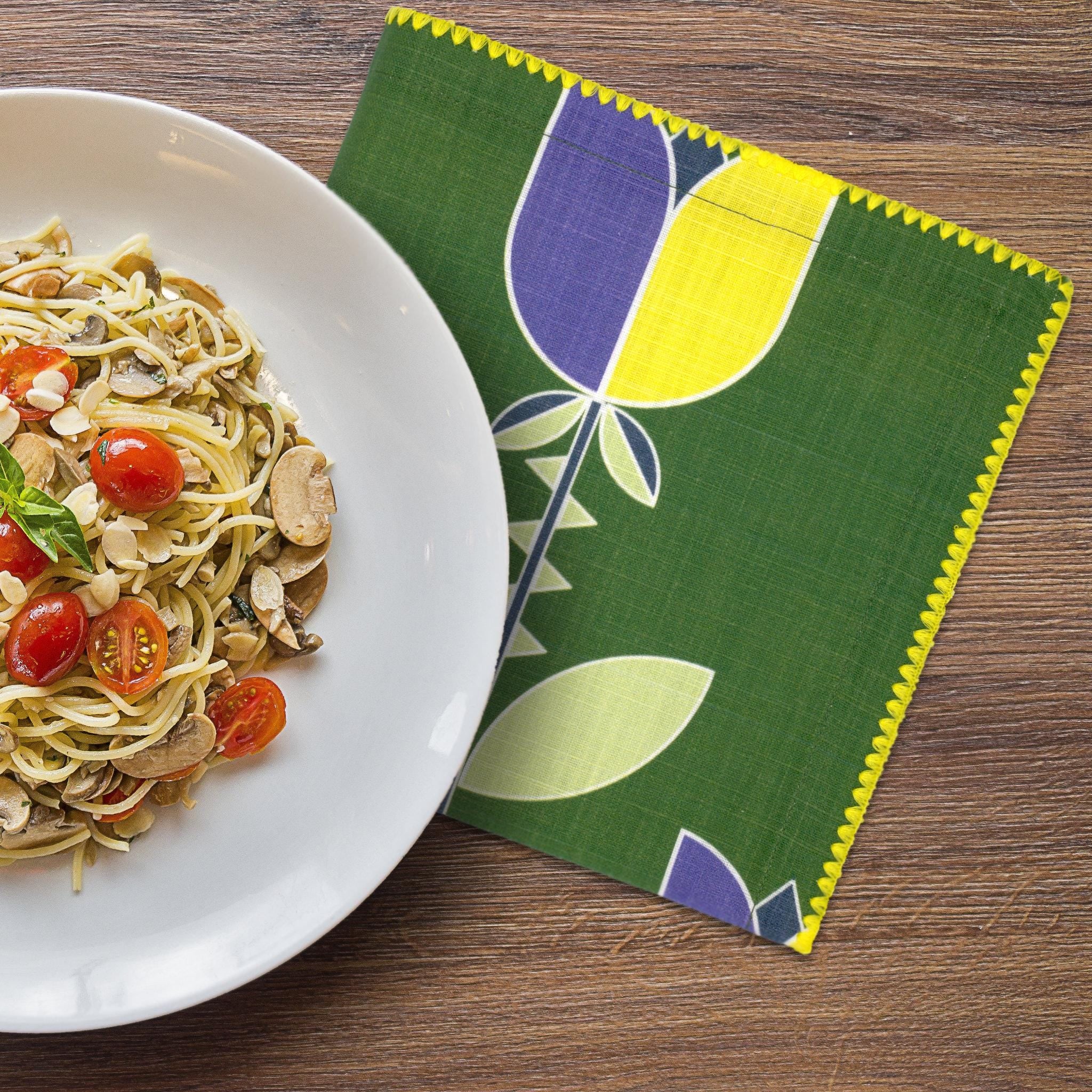 Plate of pasta with vegetables on a wooden table next to art deco lip tulip dinner napkin green on a wooden surface, from hem and tassel