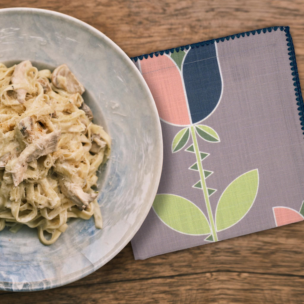 Pasta dish on a plate with a decorative art deco lip tulip dinner napkin with pasta on a wooden table