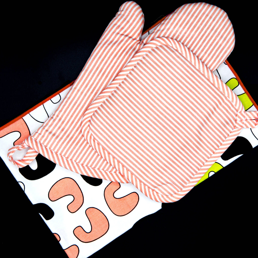 banker strip blush pot holder an oven mitt on a colorful patterned surface.from hem and tassel