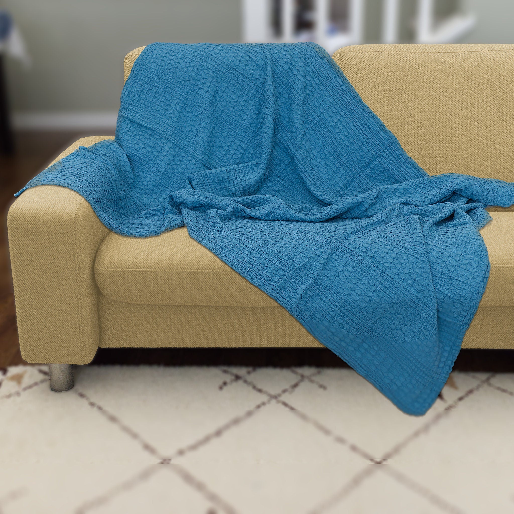 Blue textured wearable cotton throw of complex waffle weave from Hem And Tassel, draped over a beige couch in a room with tiled flooring.