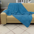 Blue textured wearable cotton throw of complex waffle weave from Hem And Tassel, draped over a beige couch in a room with tiled flooring.