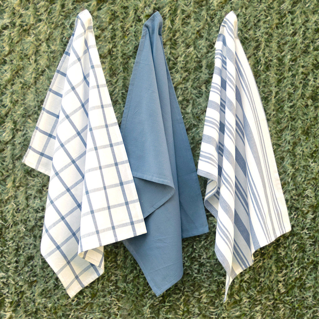 blue decade classic set of 3 kitchen towels solid, plaid and striped patterns hanging against a green grass background from hem and tassel