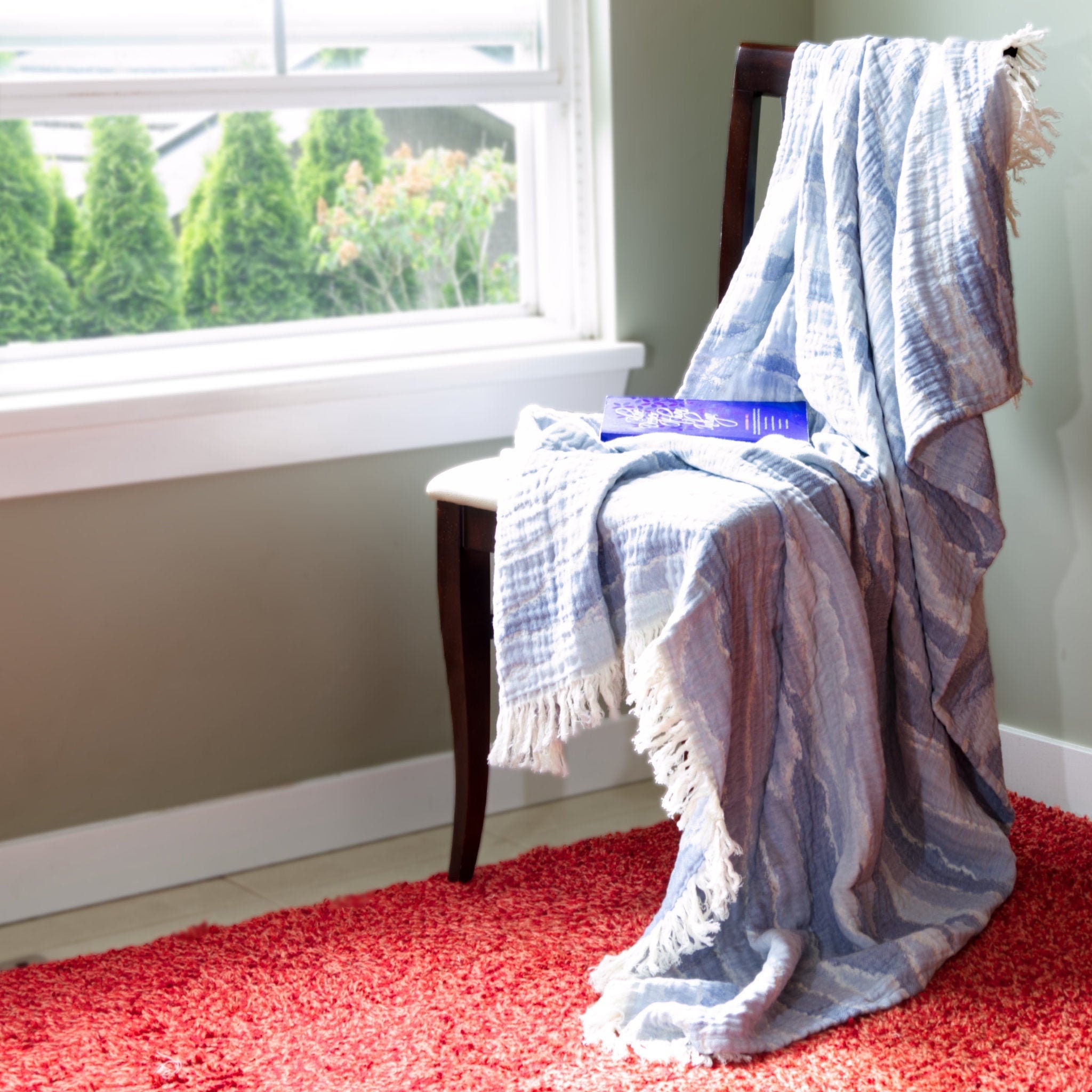 Blue striped waves pattern wearable throw blanket draped over a chair on a red rug with a window in the background