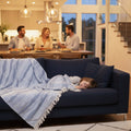 Child lying on a blue couch with a striped waves pattern throw blanket, while people are dining in the background.