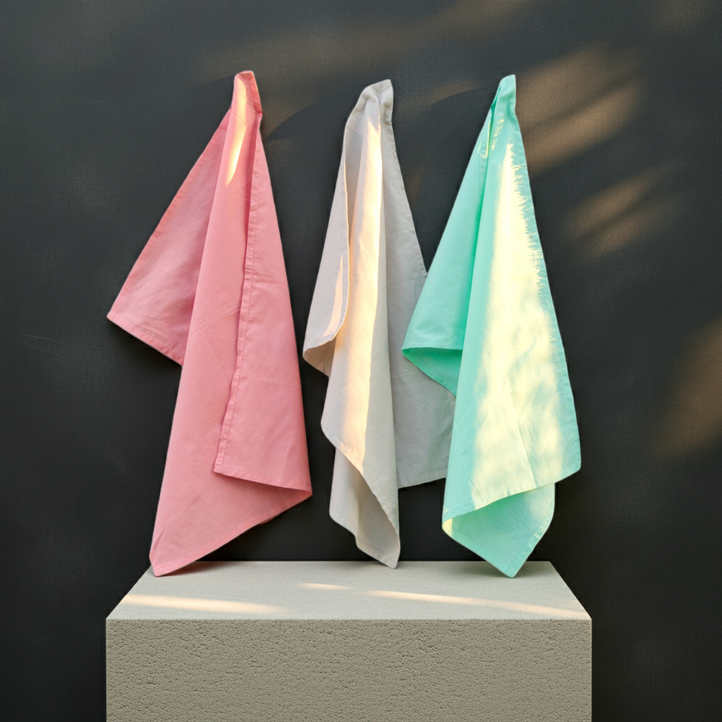 Set of three solid color kitchen towels in soft pastels hanging on a dark background from Hem And Tassel 