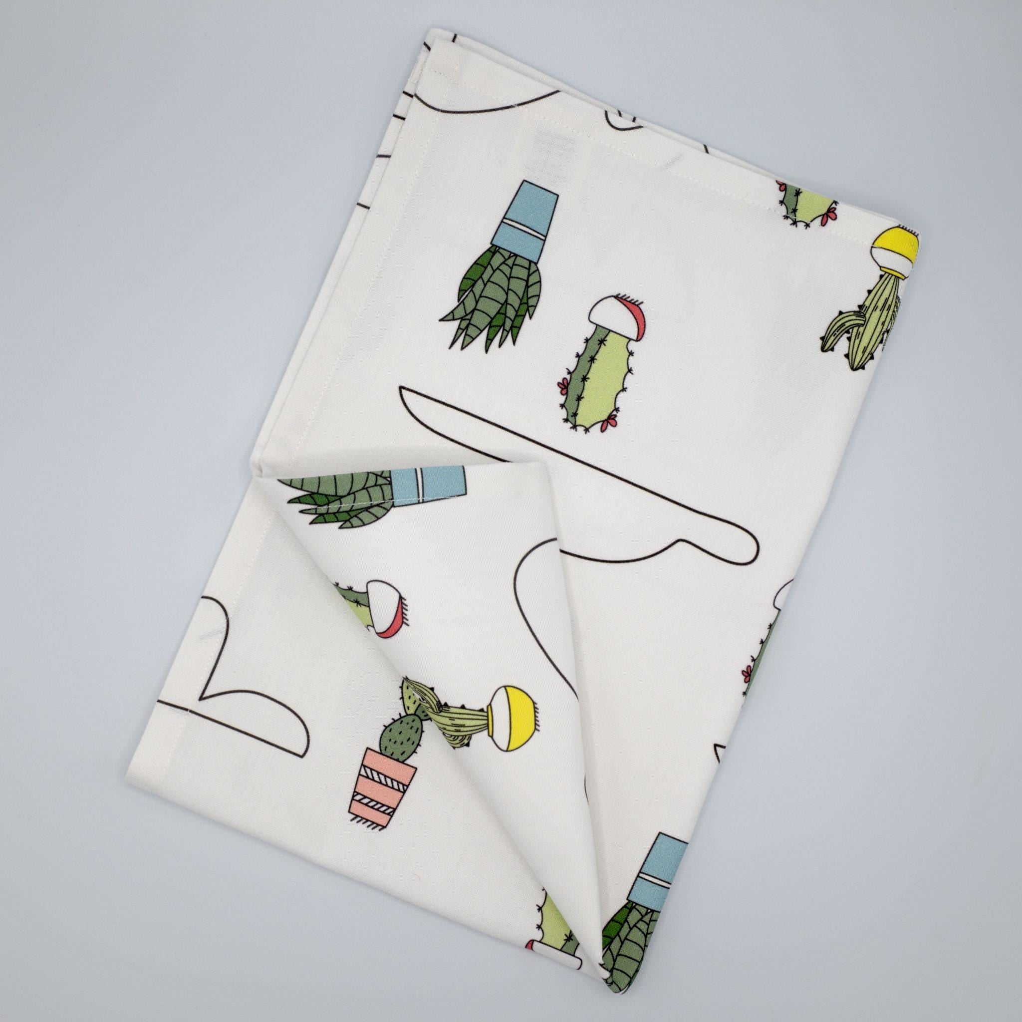 Folded tea towel with cactus and clouds pattern on a light gray background from hem and tassel