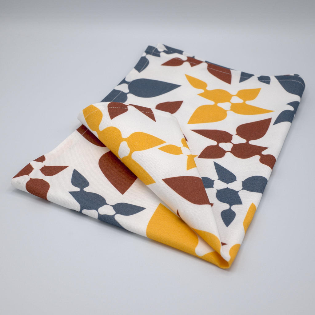 celebration tea towel folded with leaf patterns on a light gray background from Hem And Tassel 