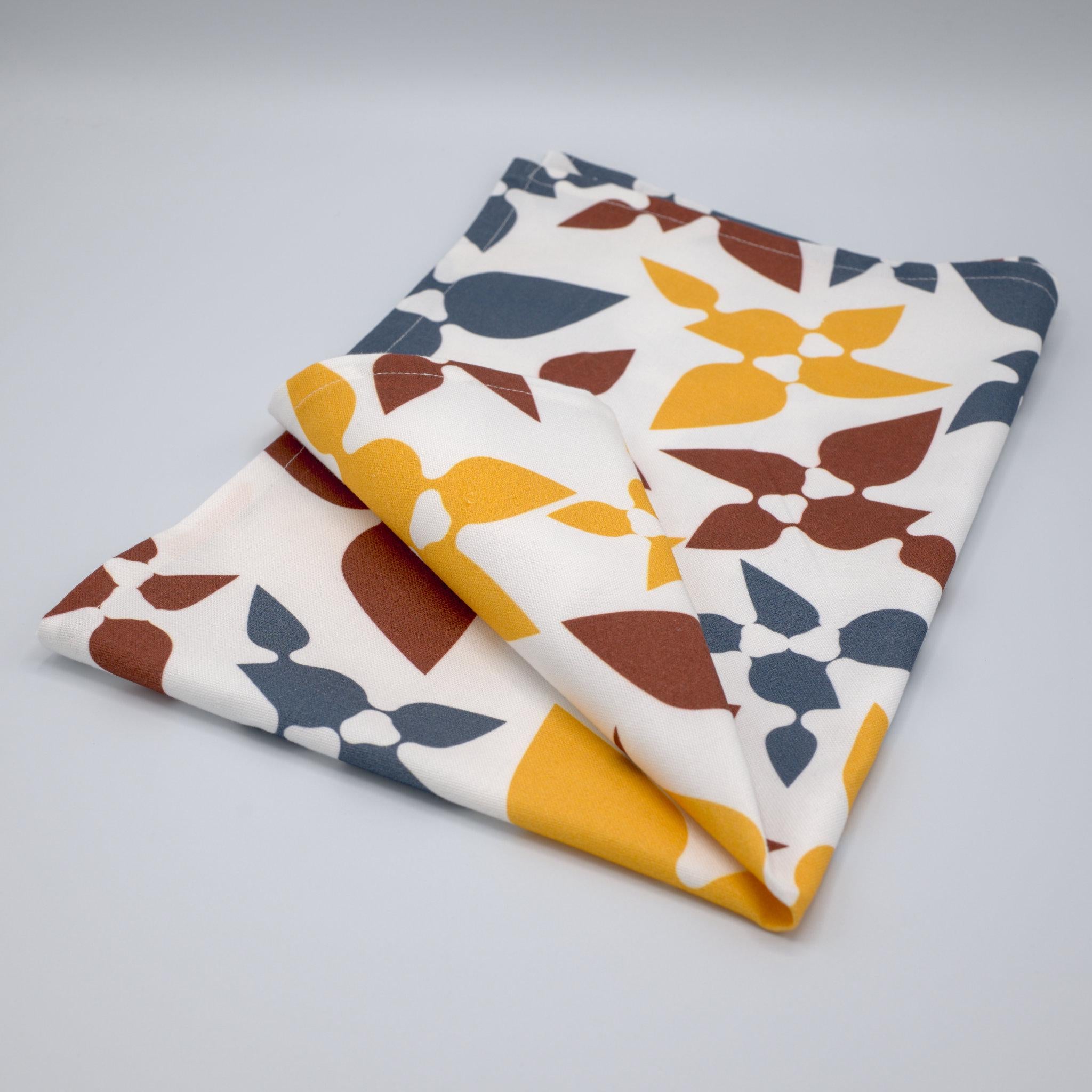 celebration tea towel folded with leaf patterns on a light gray background from Hem And Tassel 