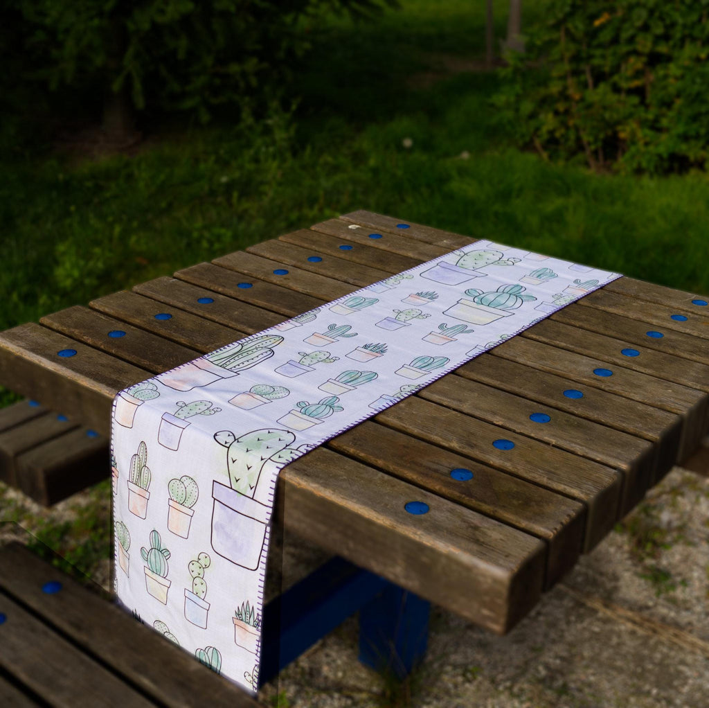 desert haze table runner with cactus pattern on a wooden table outdoors from hem and tassel