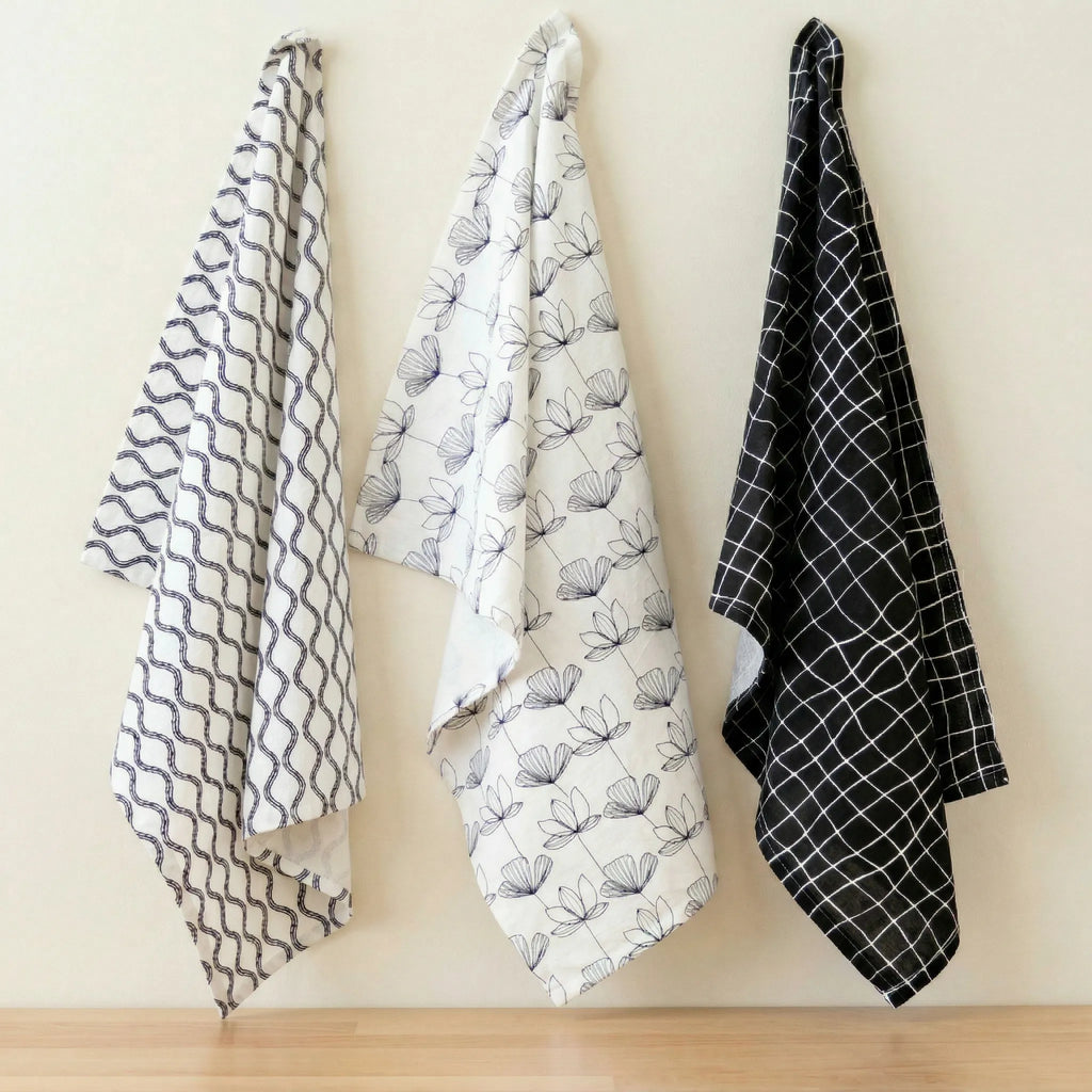 crinkled flour sack - set of three 100% cotton kitchen towels in black and white designer prints;, hanging against a cream backdrop, from Hem And Tassel