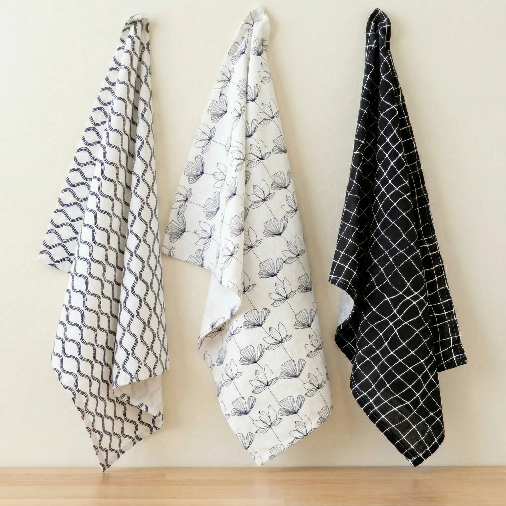 crinkled flour sack - set of three 100% cotton kitchen towels in black and white designer prints;, hanging against a cream backdrop, from Hem And Tassel