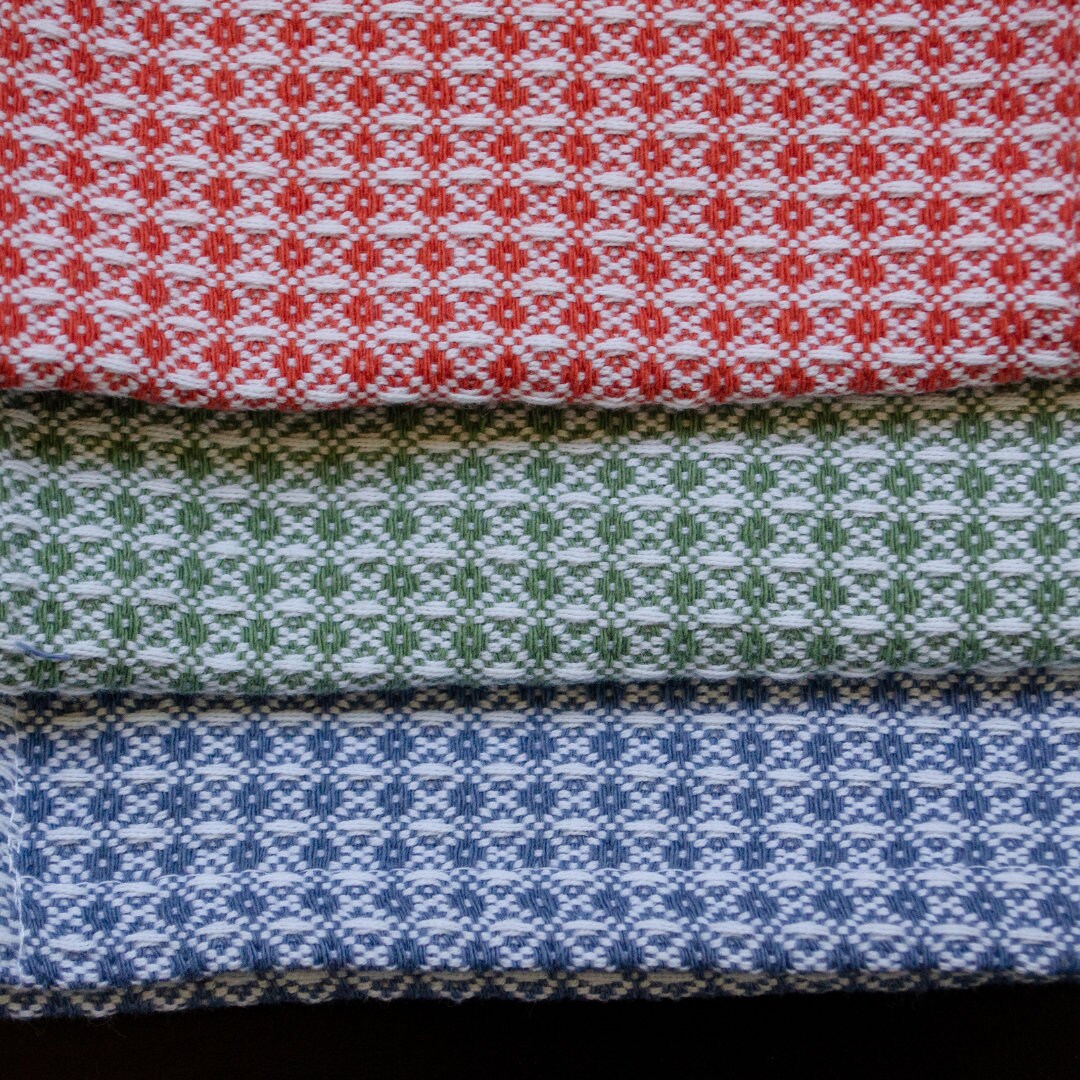 Close up of three woven diamond waffle weave wash cloth or towel samples in red, green, and blue patterns.