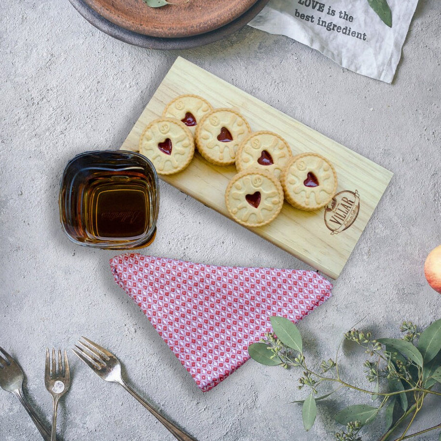 diamond waffle weave wash cloth fiolded in a triangle near wooden board with heart-shaped cookies, a small bowl of syrup, and apples on a gray surface.
