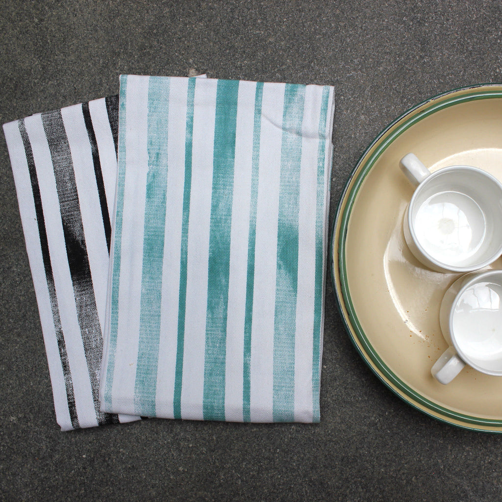 distressed Stripes kitchen towels with a plate containing two ceramic cups on a dark surface from Hem And Tassel 