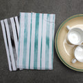 distressed Stripes kitchen towels with a plate containing two ceramic cups on a dark surface from Hem And Tassel 