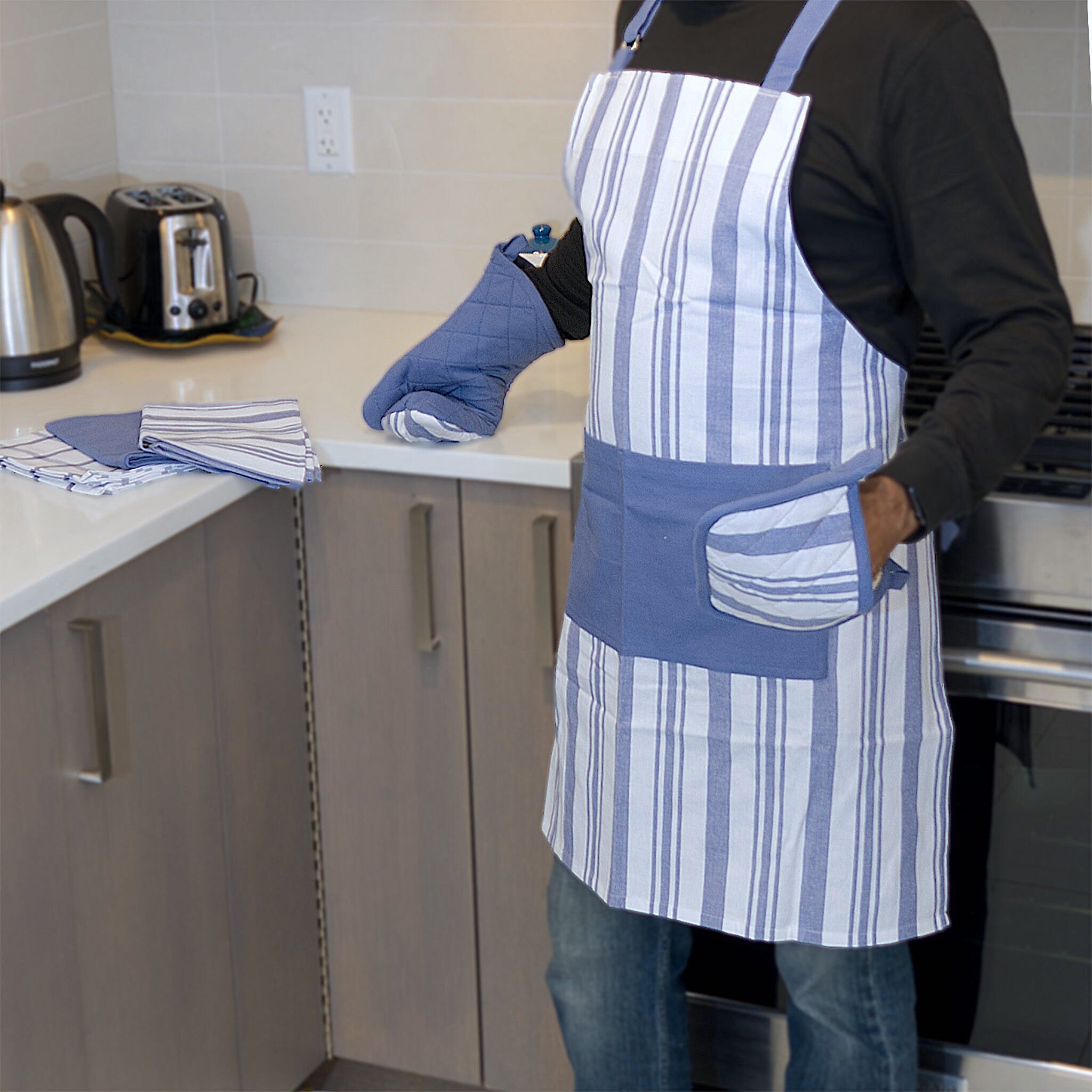 everyday classic striped cotton Apon in blue stripes on white, from Hem And Tassel on person in kitchen with matching towels, oven mitt and pot holder