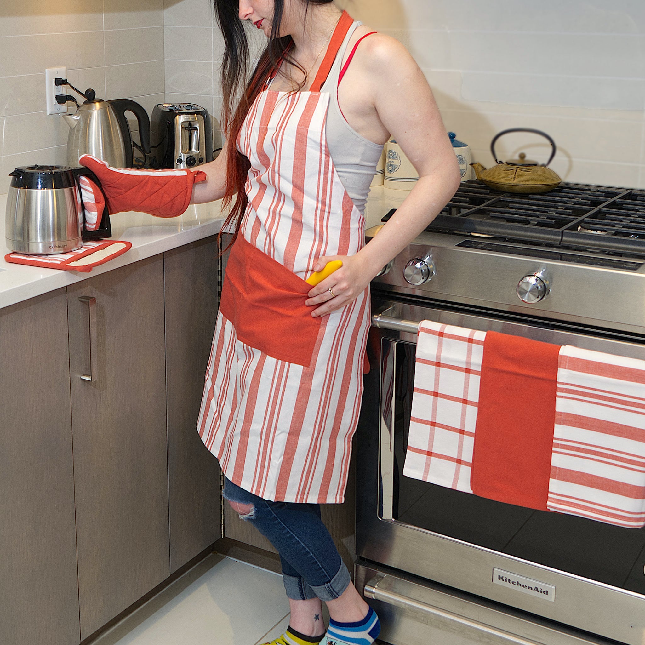 everyday classic striped cotton Apon with red stripes on white, from Hem And Tassel on person in kitchen with matching towels, oven mitt and pot holder also on counter